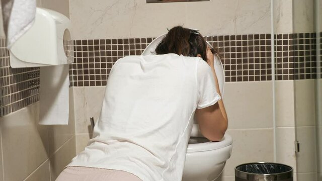 unrecognizable young woman bent over the toilet, poisoning, toxicosis.