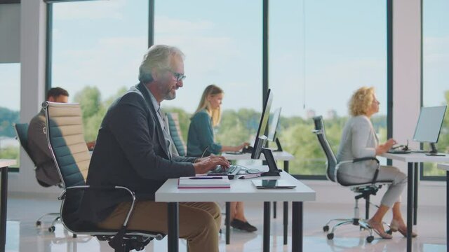Slide and pan shot of morning work in shared office. Modestly furnished room with large windows. Modern open space office interior.