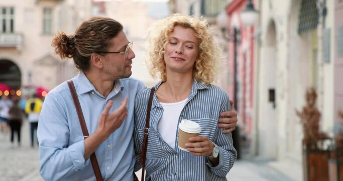 Waist up portrait view of the caucasian couple in love embracing while walking through the city at the summer day. Relationships concept