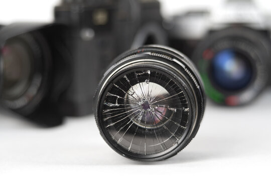 Broken camera lens with blurred photography equipment background, selective focus