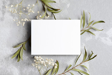 Wedding invitation card mockup with eucalyptus and gypsophila twigs. Blank card mockup on grey background.