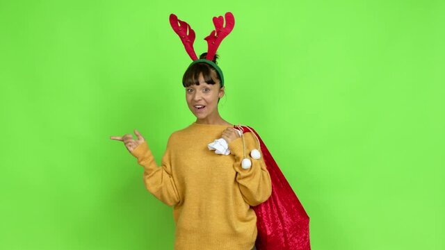 Young woman with christmas hat pointing to the side and presenting a product while smiling over isolated background. Green screen chroma key