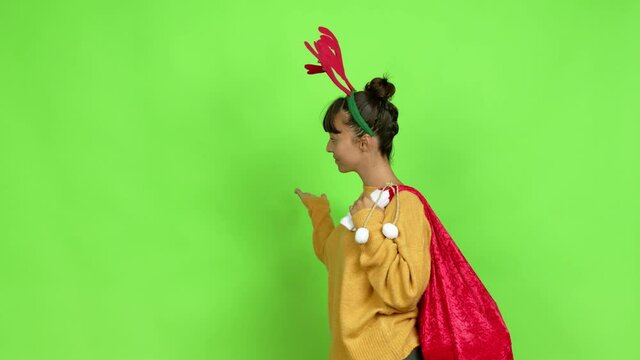 Young woman with christmas hat pointing back and presenting a product over isolated background. Green screen chroma key