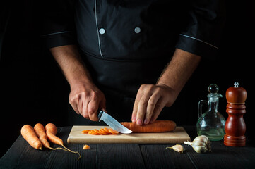 The chef is cutting carrots for vegetable soup in the restaurant kitchen. Close-up of the hands of the cook during work. Carrot diet