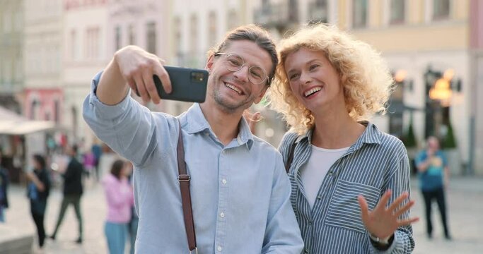 Happy selfie. Waist up portrait view of the caucasian man and woman in love posing and gesturing while making selfie at the street