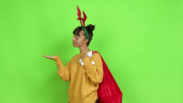 Young woman with christmas hat extending hands to the side and inviting to come over isolated background. Green screen chroma key