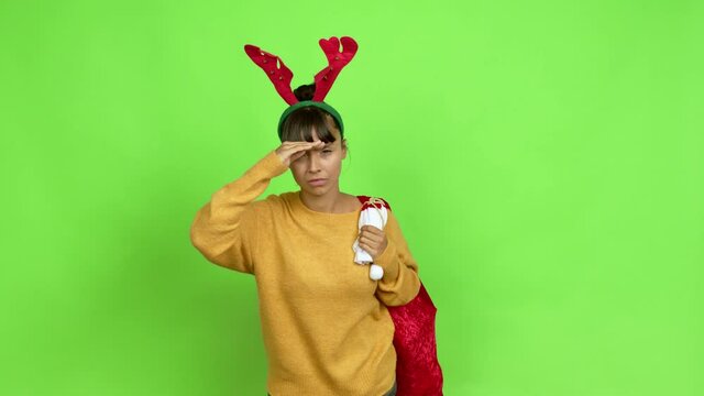 Young woman with christmas hat looking far away with hand to look something over isolated background. Green screen chroma key