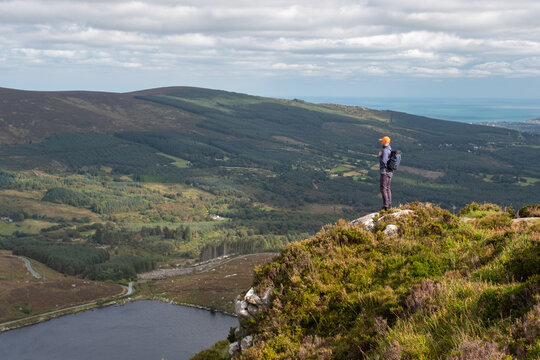 Man with backpack standing on the edge of the cliff over Lough Bray in Wicklow Mountains, Ireland. September 2021