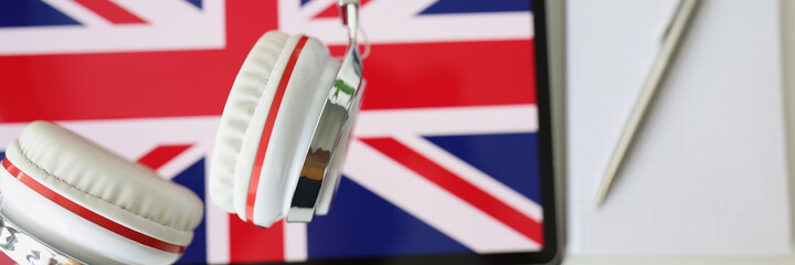 Tablet with image of British flag with headphones and notebook with pen lie on table