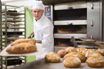 male baker with bread on baking shovel in kitchen
