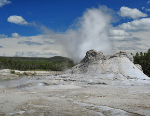 geyser blows under cloudy blue skies in Yellowstone national park
