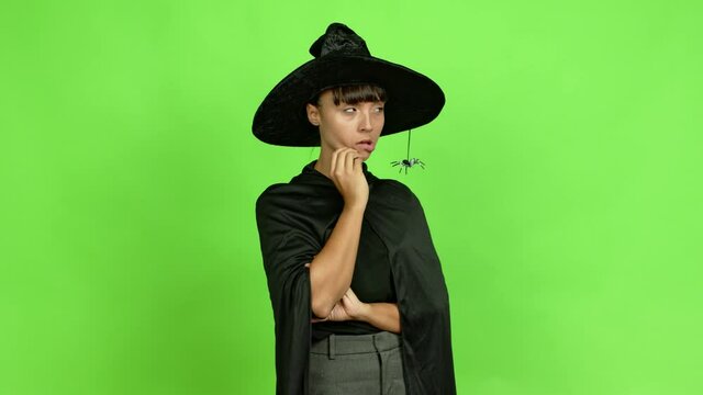 Young woman wearing witch hat having doubts and questioning an idea over isolated background. Green screen chroma key