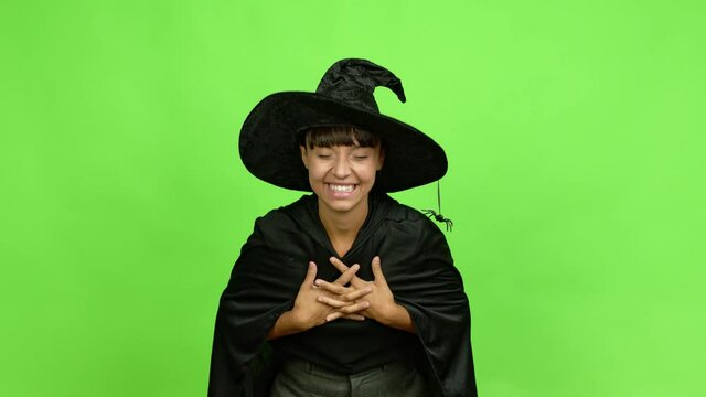 Young woman wearing witch hat smiling a lot while covering mouth over isolated background. Green screen chroma key