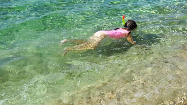 Toddler girl learning snorkeling on shallows. Child immersing the head in water. Kids diving with snorkel mask and tube on the water s edge. Family vacation concept