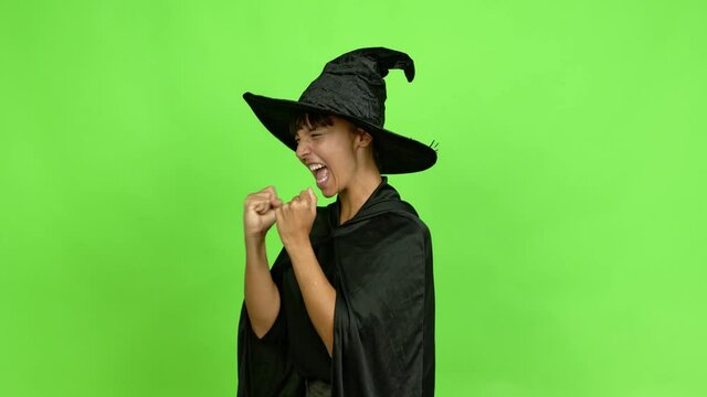 Young woman wearing witch hat for halloween parties celebrating a victory over isolated background. Green screen chroma key