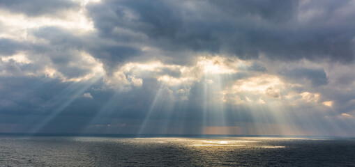 The sun breaks through the clouds illuminating the sea with its rays  - Powered by Adobe