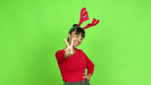 Young woman wearing christmas hat smiling and showing victory sign with a cheerful face over isolated background. Green screen chroma key