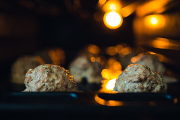 View into the oven on the baking tray for meatballs. Little light, light only from the oven. Shallow depth of field, blurred background.