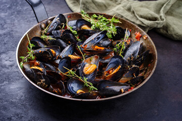 Traditional barbecue Italian blue mussel in tomato red wine sauce with herb and garlic as close-up in a rustic iron pan