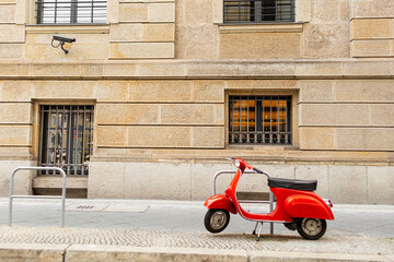 Fototapeta na wymiar A stylish red moped is parked on a plain street. A bright spot in the city