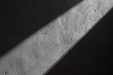 A shaft of light beams down across a textured concrete basement wall