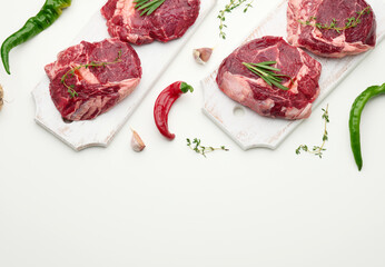 raw piece of beef ribeye with rosemary, thyme on a white table, top view