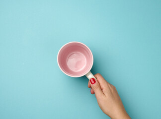 female hand holds a ceramic mug on a blue background, break time and drink coffee