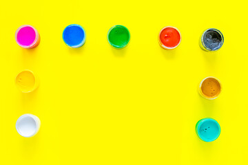Cans of multi-colored paint are located on the side and on top of the photo on a yellow background. top view, flat lay, copy space, isolate.