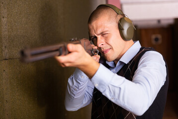 Concentrated man wearing protective earmuffs practicing shotgun shooting at firing range.