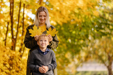 Mother and son have fun together. Family walk in the park in autumn. Hello October. Thanksgiving holiday. Happy motherhood. Childhood. Maple leaves. Fun play together. Leaf ears. Fall