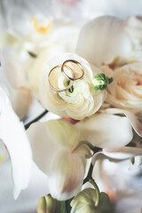 wedding rings lie on a bouquet of flowers of roses and orchids close-up top view