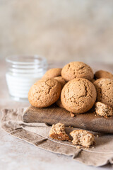 Oatmeal cookies on wooden cutting board with a cup of milk, brown concrete background. Healthy snack or dessert.