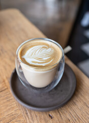 Coffee with latte art in cup on wooden table in cafe or coffee shop.