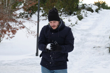 Fototapeta na wymiar Young caucasian man making a snowball in a park