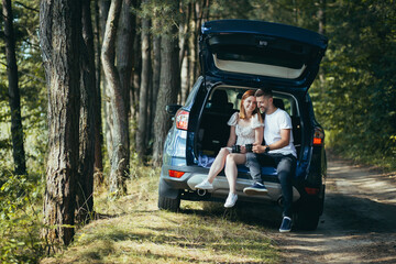 Young couple, man and woman, hugging together on a picnic, sitting in the trunk of a car in the woods, happy together