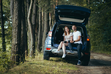 Young couple, man and woman, hugging together on a picnic, sitting in the trunk of a car in the woods, happy together