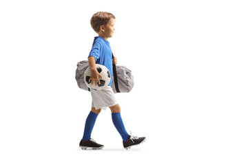 Full length profile shot of a boy wearing a sports jersey, holding a soccer ball and bag and walking