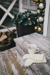 Mug with hot coffee or cocoa on terrace of house decorated with Christmas garland and festive lights.