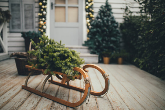 Door Of Wooden House Decorated With Festive Lights And Chrismas Wreath. Sled With Pine. Holiday House Decoration.