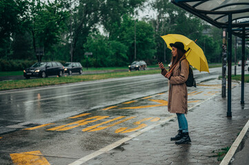 Woman using a smartphone and holding a yellow umbrella in the city