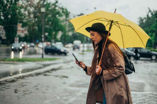 Woman using a smartphone and holding a yellow umbrella in the city