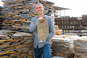 Young man salesperson checking quality of natural stone tiles at hardware store warehouse