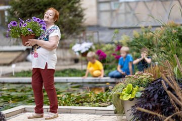 elderly woman chooses flowers in botanical garden. Three grandchildren are watching her