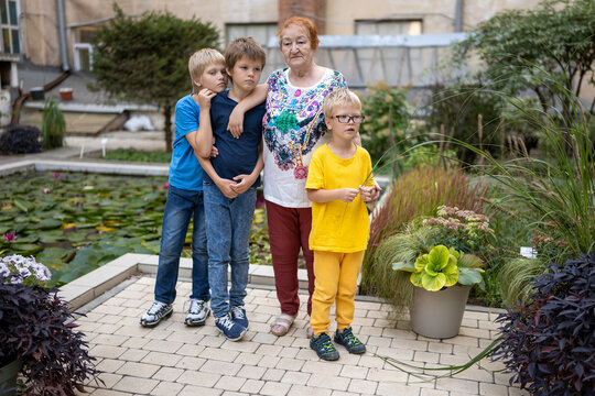 elderly woman chooses flowers in botanical garden. Three grandchildren in bright clothes stand next to her