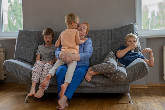 elderly woman peeks into smartphones of children sitting on sofa surrounded by grandchildren