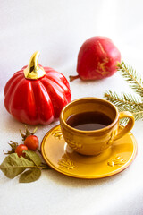 Red jack o lantern pumpkin, Halloween, Thanksgiving day. Small yellow ceramic cup with black coffee on saucer stands on white table top view. Autumn leaves, rosehip berries, spruce branch, red pear.