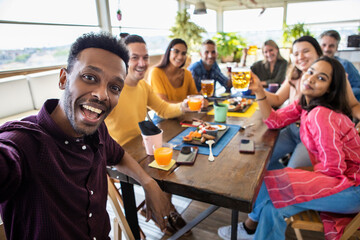 Happy group of multiracial people taking a selfie while having breakfast together on rooftop cafe...
