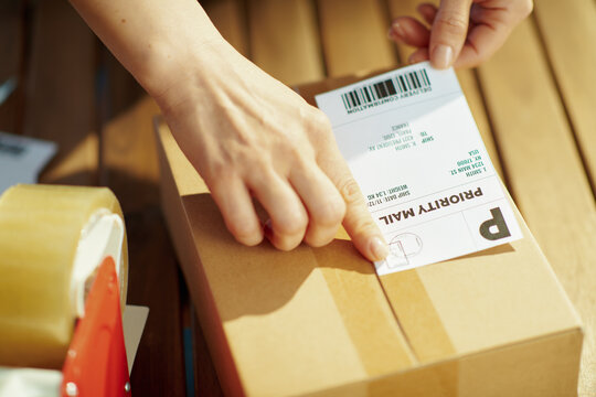 Modern female in warehouse applying shipping label to parcel