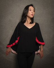 Woman of Asian descent with long dark hair and a calm demeanor poses for the camera in dark...