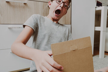Excited boy sitting on a carpet and opening a box, a parcel, unboxing and unpacking concept